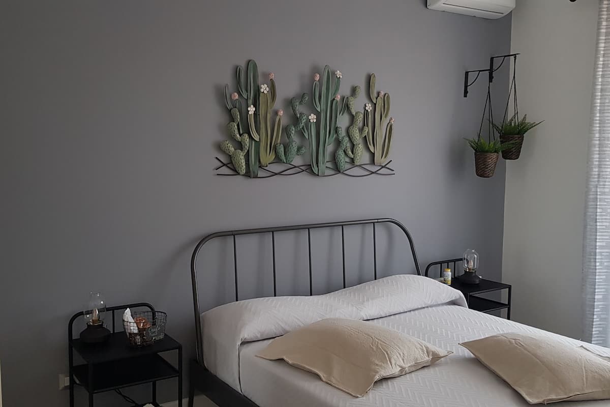 Une chambre à coucher avec un lit, deux tables de chevet, une décoration murale en forme de cactus et une plante suspendue.