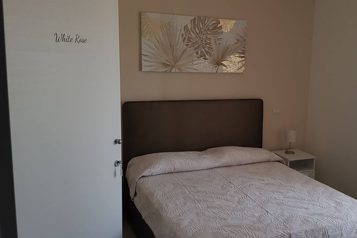 Une chambre à coucher comprenant un lit, une table de chevet, une lampe et une œuvre d’art murale.