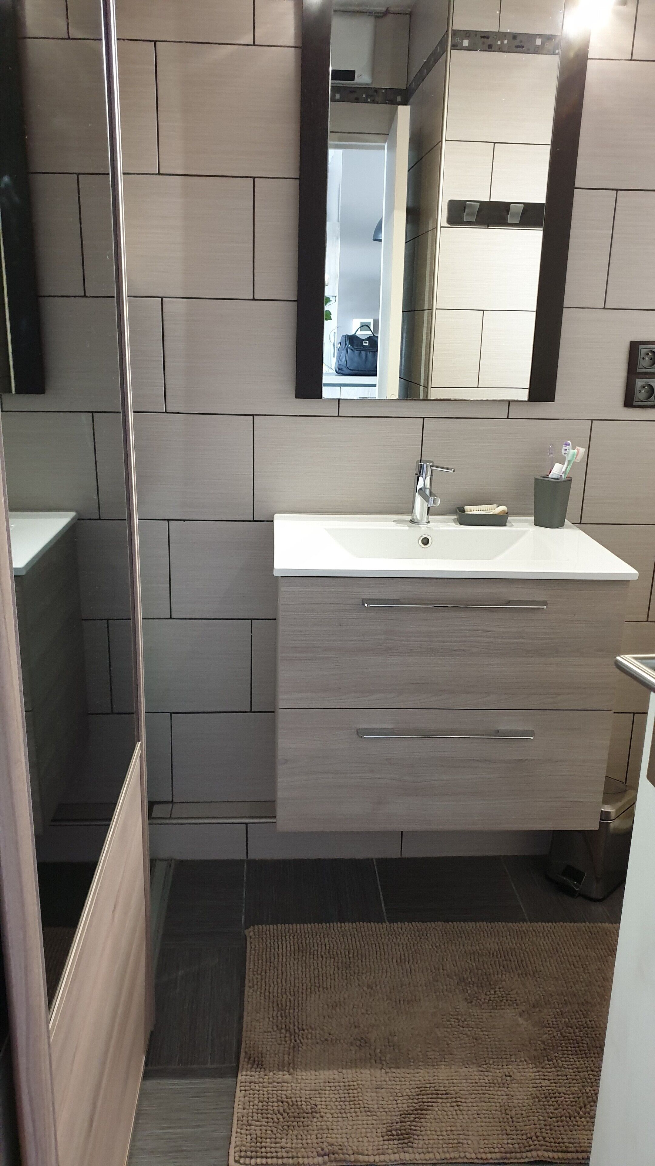 Un baño moderno con un lavamanos blanco, tocador de madera y un espejo encima.
