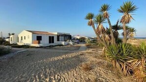 A white building with a flat roof, surrounded by sand dunes and palm trees. - Casa W Olhão - ALMIRANTE (Olhão)