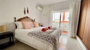 A bedroom with a bed, pillows, a bedside table, and a window with curtains. - Casa W Olhão - ALMIRANTE (Olhão)