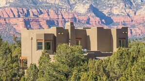 Un edificio moderno con tetto piano e ampie finestre, immerso tra alberi e con montagne sullo sfondo.