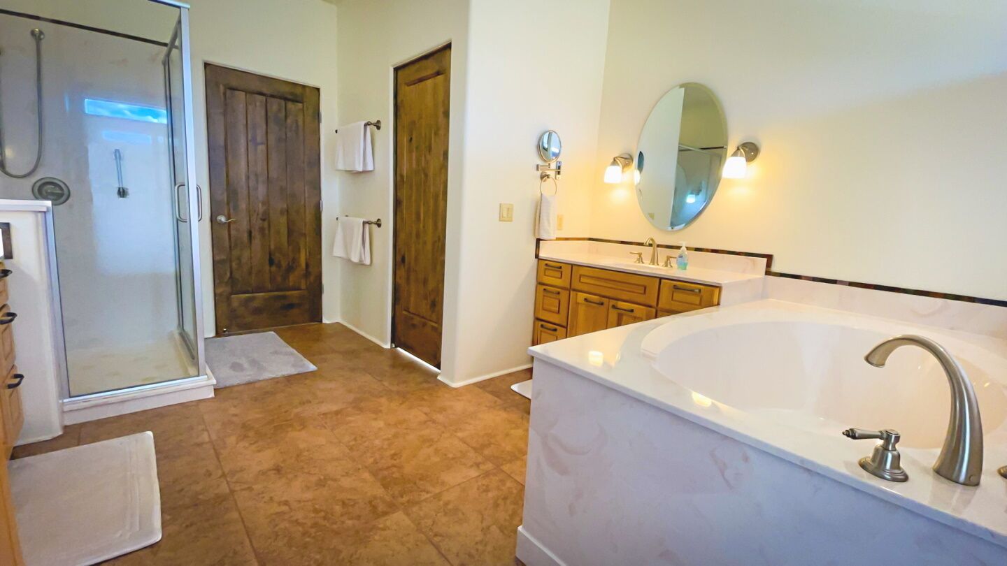 A bathroom with a glass shower enclosure, a wooden door, a white bathtub, and wooden cabinets.