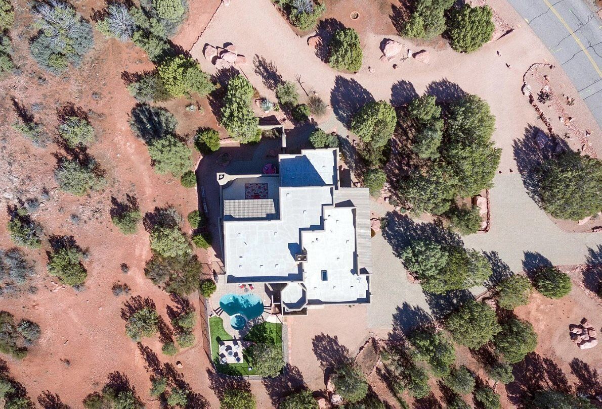 An aerial view of a house with a large patio, surrounded by trees and a swimming pool.