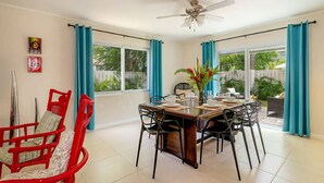 A dining area with a table set for four, surrounded by chairs, a ceiling fan, and large windows with curtains. - Hospitality Expert CP (Montego Bay)