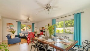 A dining area with a wooden table, black chairs, and a ceiling fan. There is a sofa and a dining table set with plates, bowls, and cups. - Hospitality Expert CP (Montego Bay)