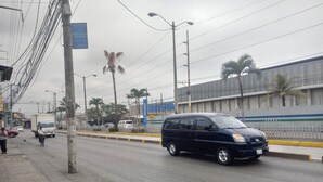 Una calle con una camioneta azul, palmeras y un edificio con un letrero que dice 'UNIVERSO'.