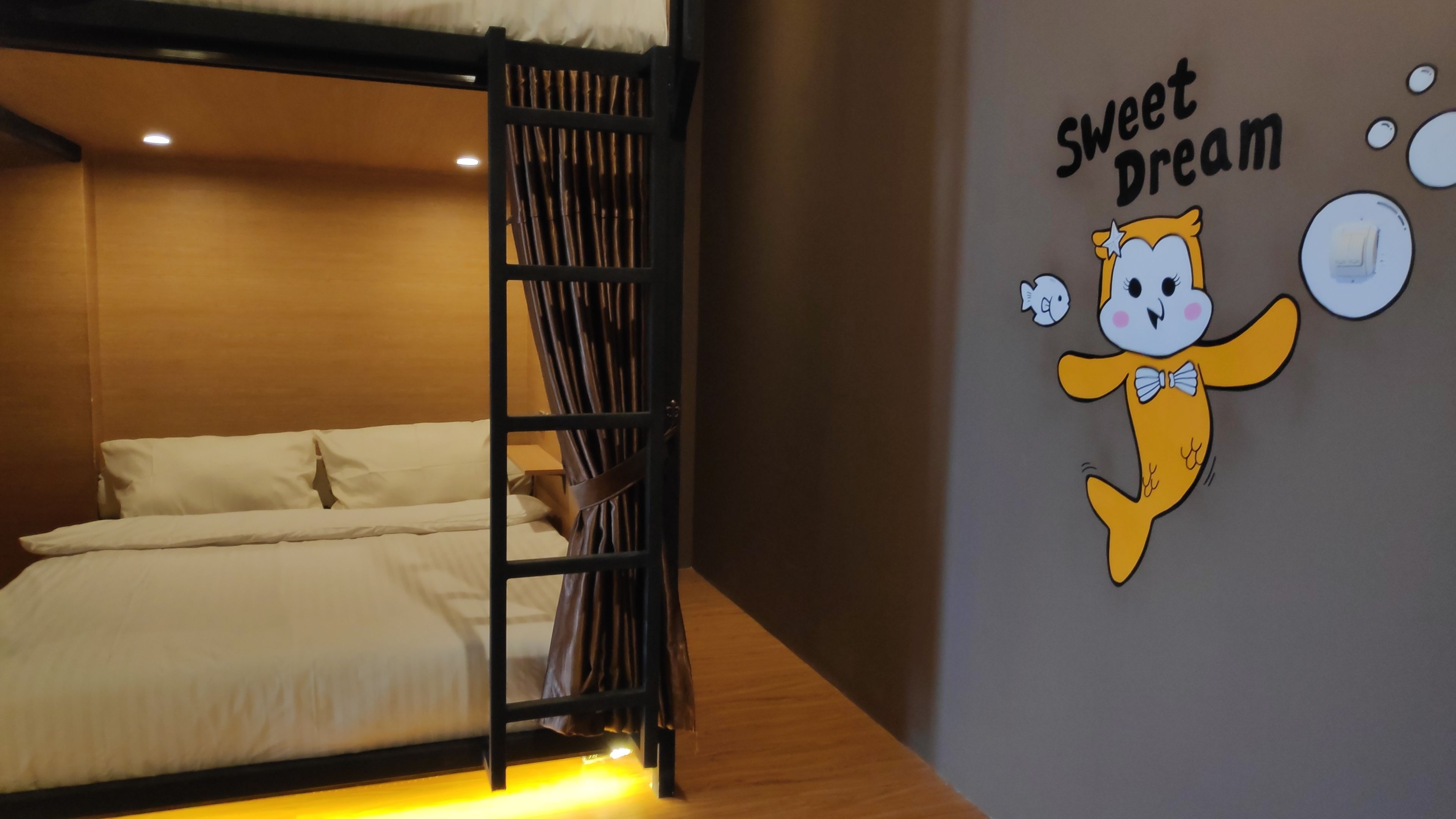 A bunk bed with a wooden ladder, white bedding, and a wall with a cartoon character and the text "Sweet Dream".