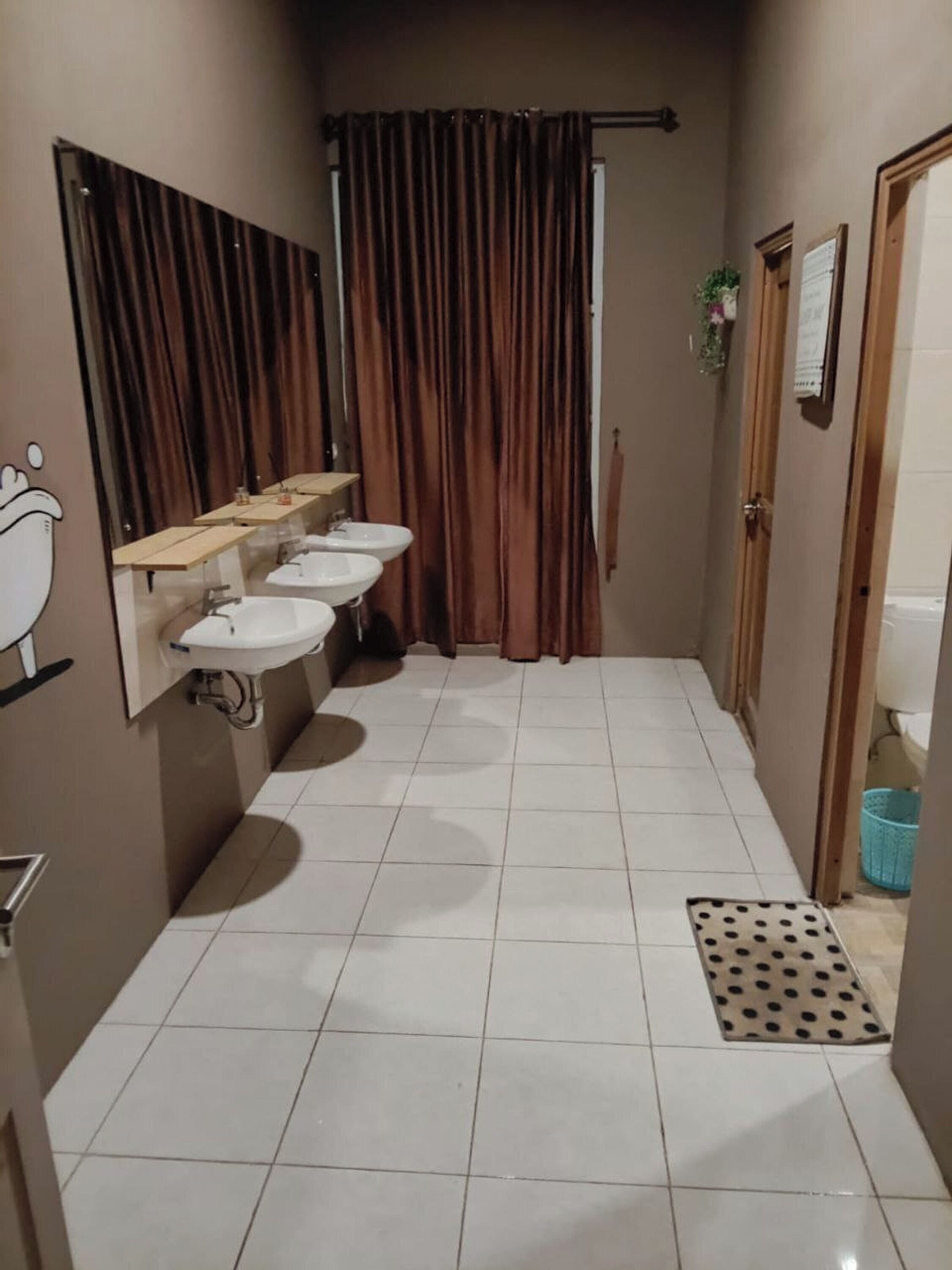 A narrow bathroom with three sinks, a mirror, and a shower curtain.