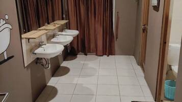 A narrow bathroom with three sinks, a mirror, and a shower curtain.