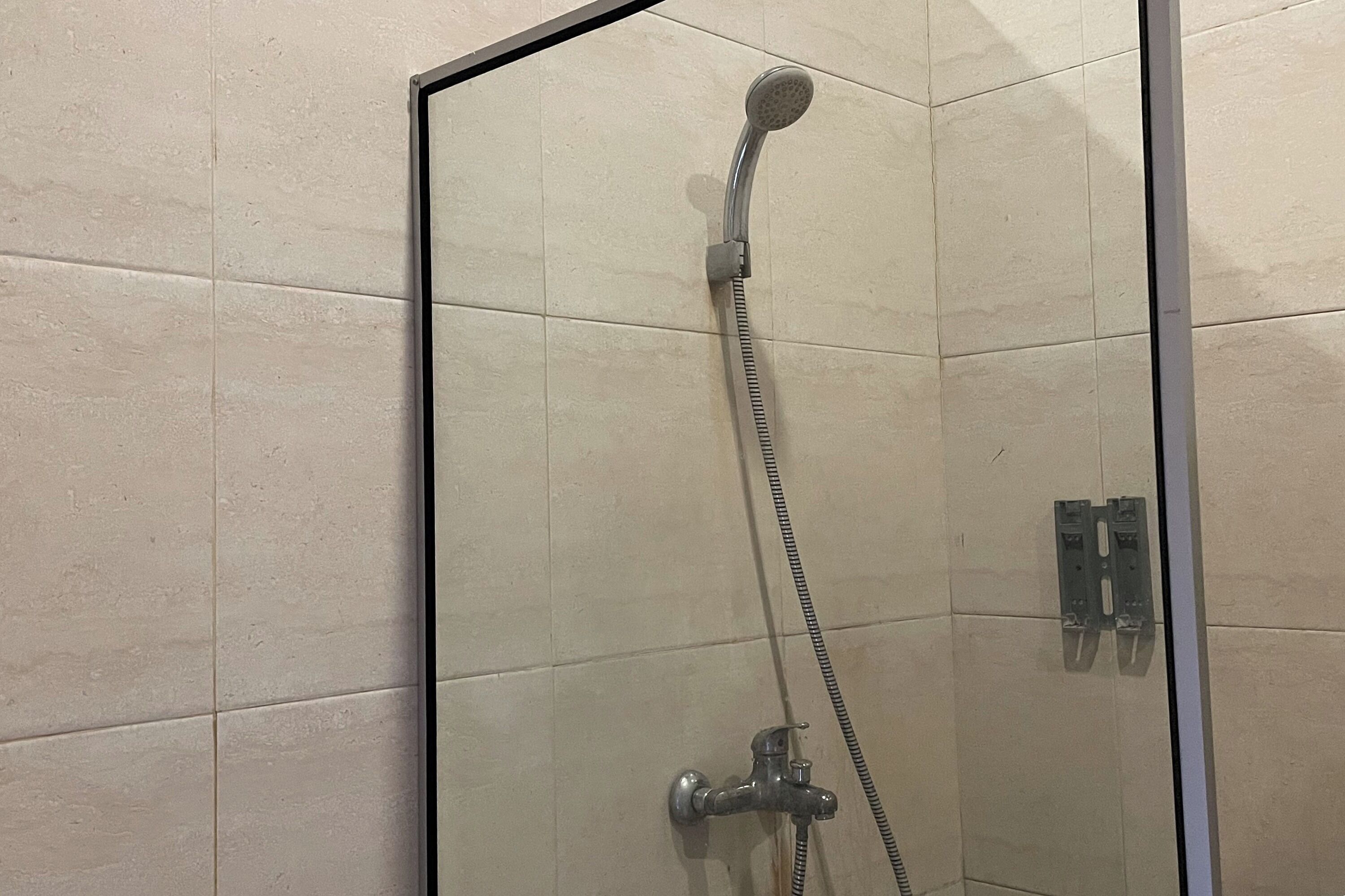 Une douche fermée par des parois en verre, dotée d’un pommeau de douche à main et d’un robinet mural.