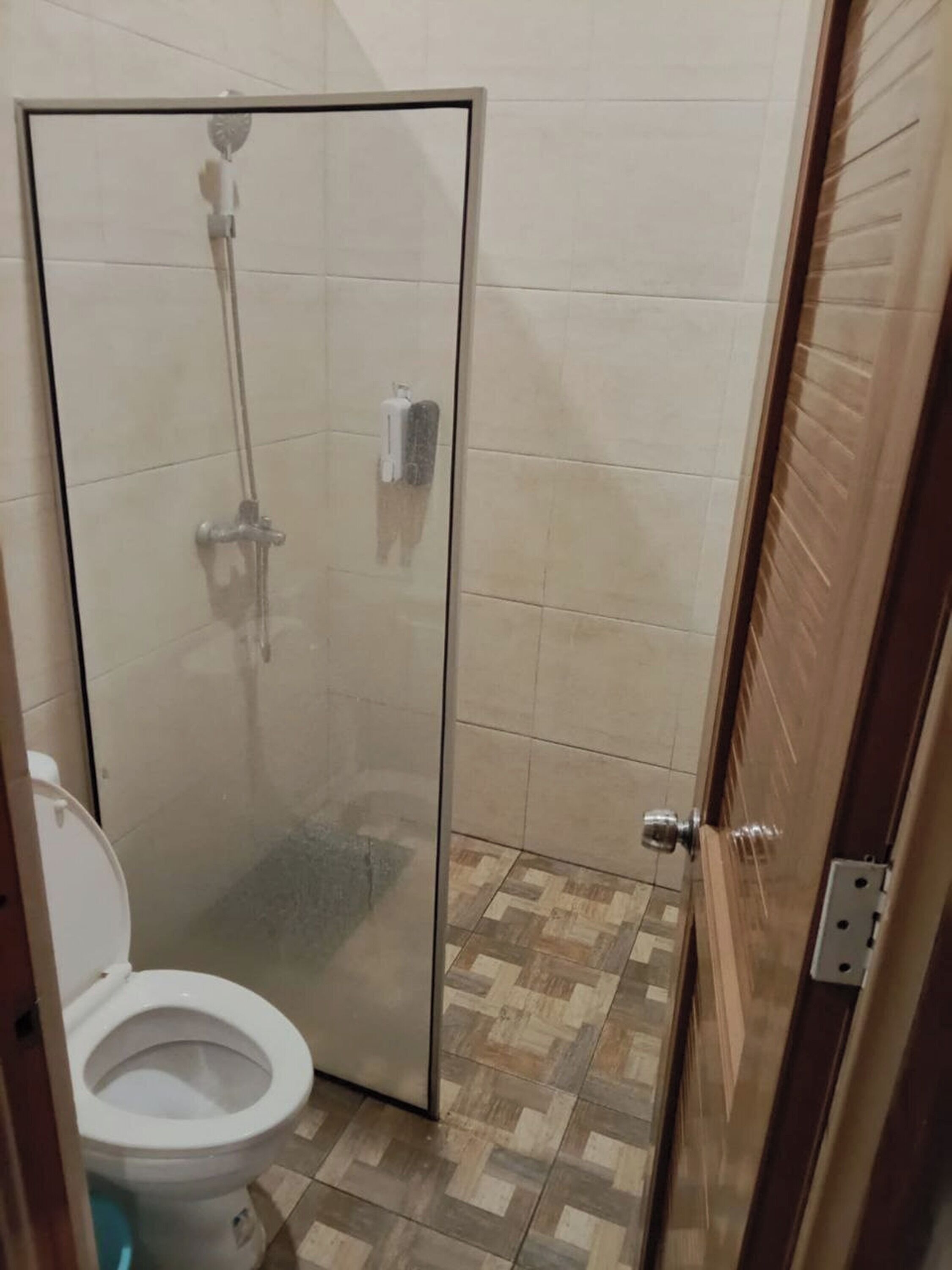 A small bathroom with a glass shower enclosure, a toilet, and a tiled floor.
