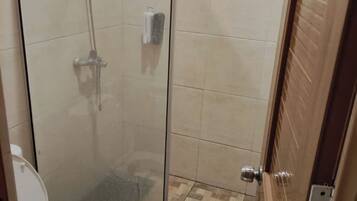 A small bathroom with a glass shower enclosure, a toilet, and a tiled floor.