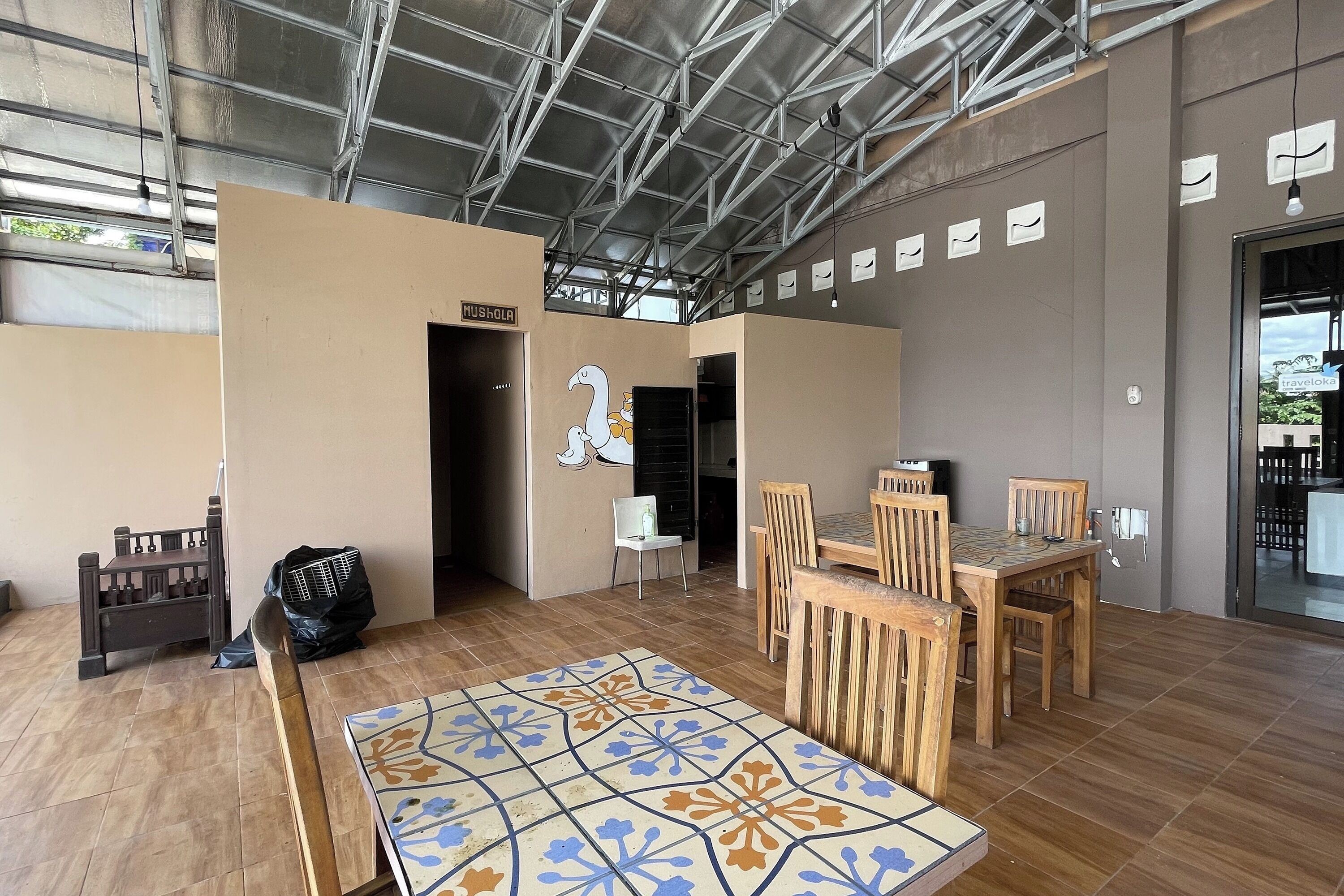 A spacious indoor area with a high ceiling, a tiled floor, and a seating area with wooden tables and chairs.
