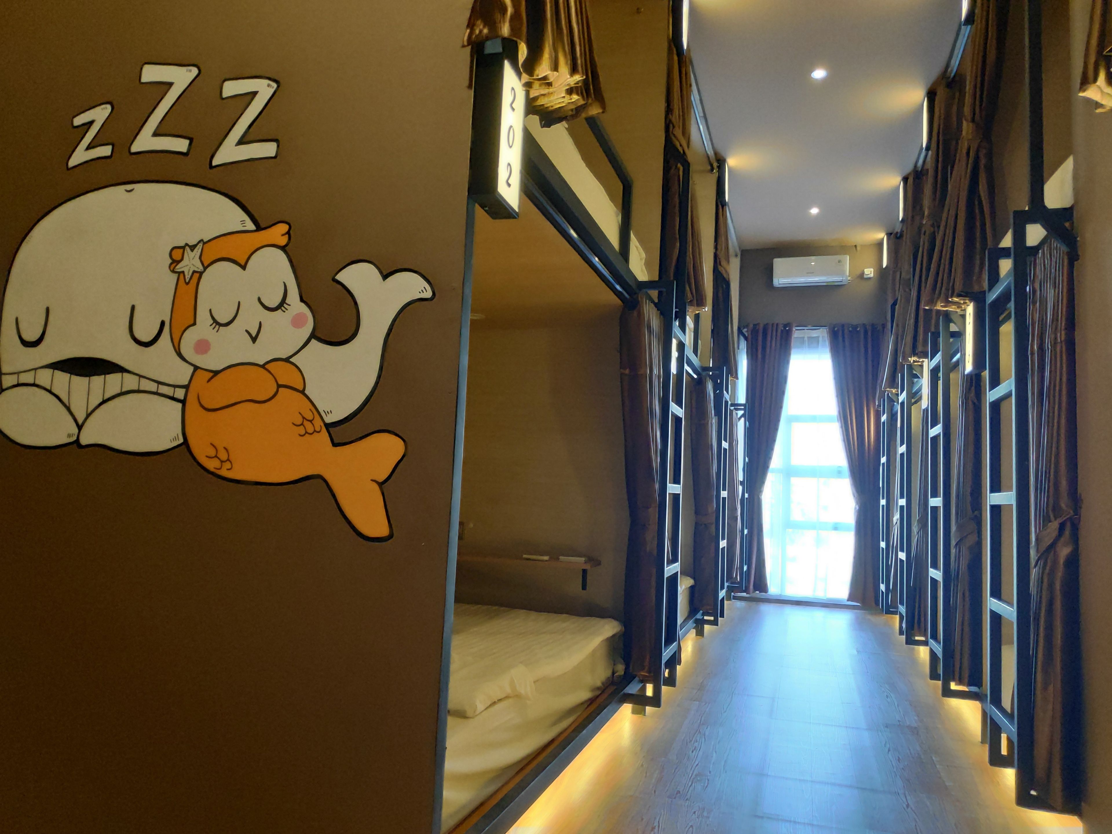 A hotel corridor with bunk beds, a cartoon character on the wall, and a window at the end.