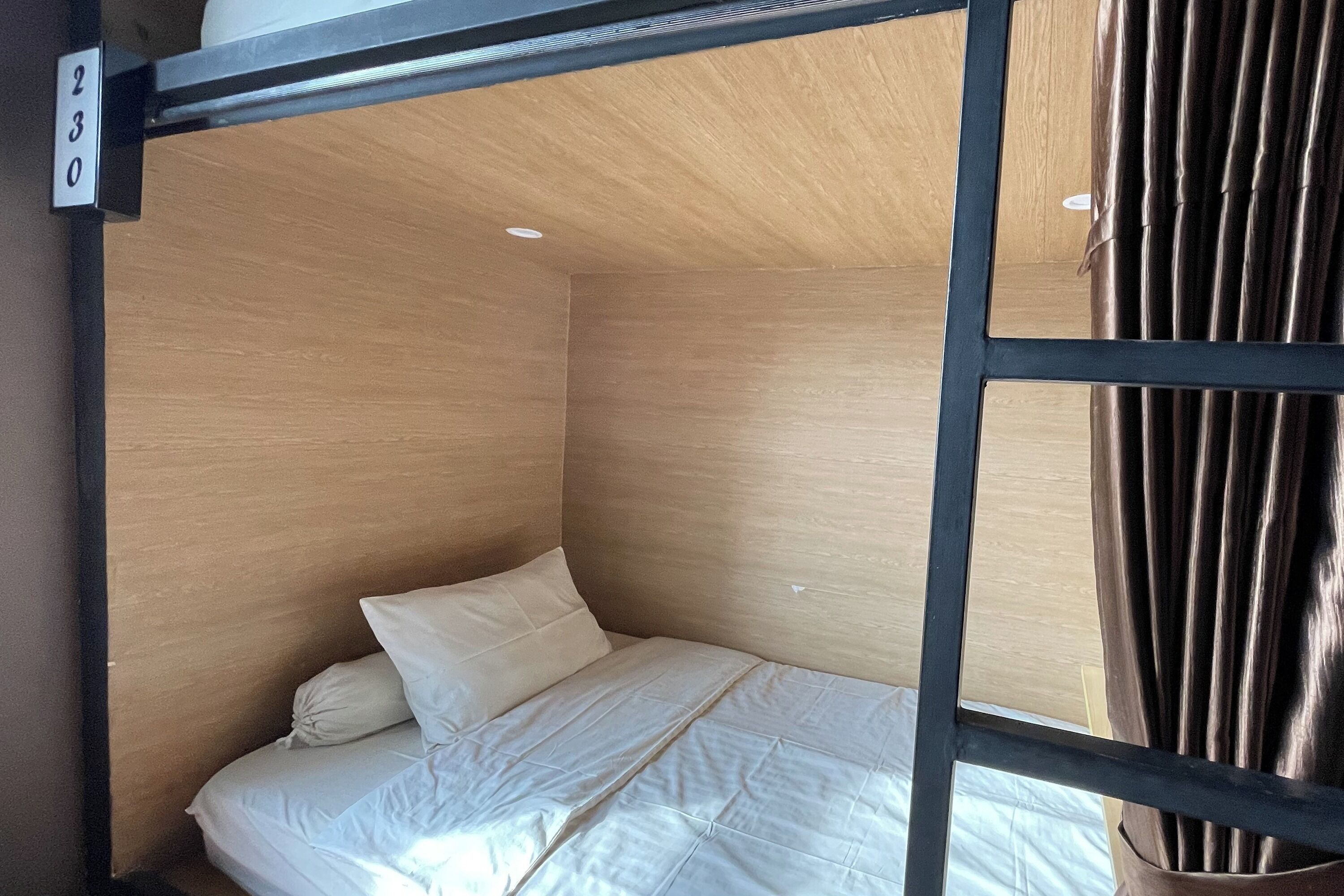 A compact room with a single bed, a wooden ceiling, and a metal frame.