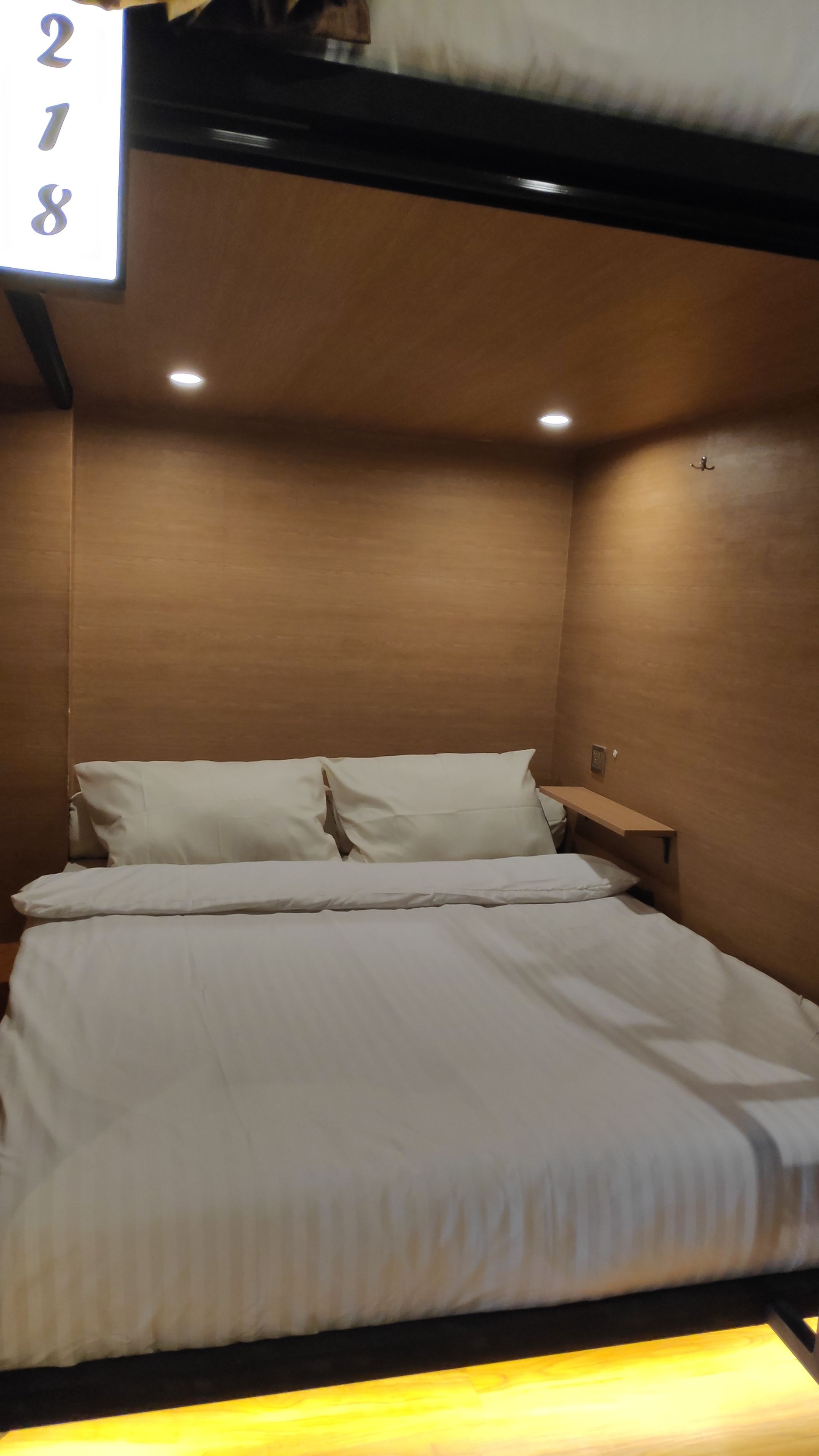 A neatly made bed in a room with wooden walls and a small bedside table.