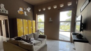 Eine Hotelhalle mit einer Couch, gelben Schließfächern, einem Fernseher und Blick ins Freie.