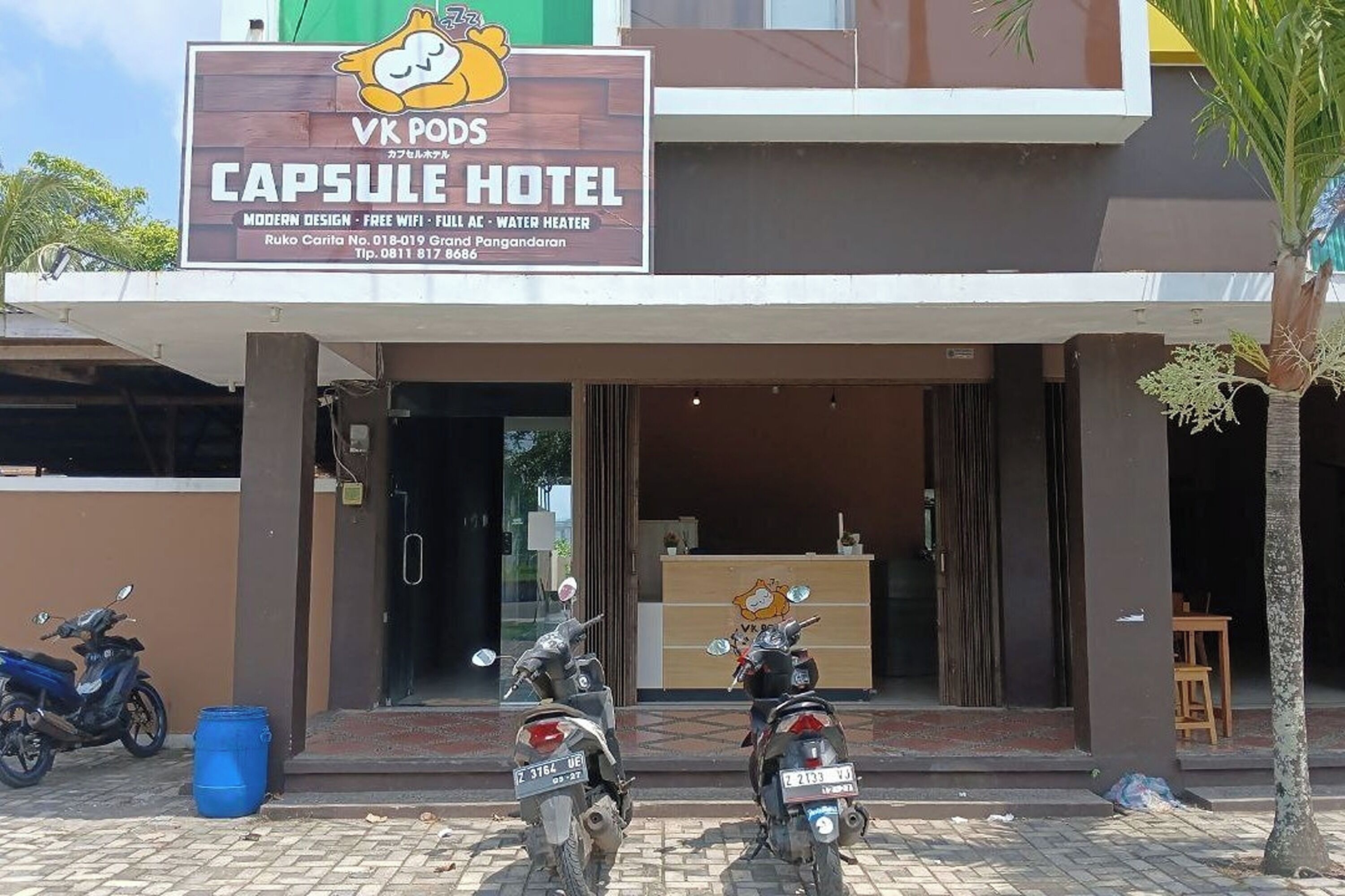 L’entrée d’un hôtel, avec une enseigne indiquant « VK Pods Capsule Hotel », un design moderne, une connexion Wi-Fi gratuite, la climatisation et un chauffe-eau.