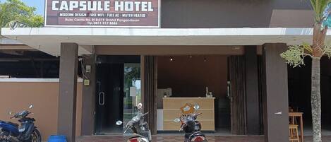 L’entrée d’un hôtel, avec une enseigne indiquant « VK Pods Capsule Hotel », un design moderne, une connexion Wi-Fi gratuite, la climatisation et un chauffe-eau.