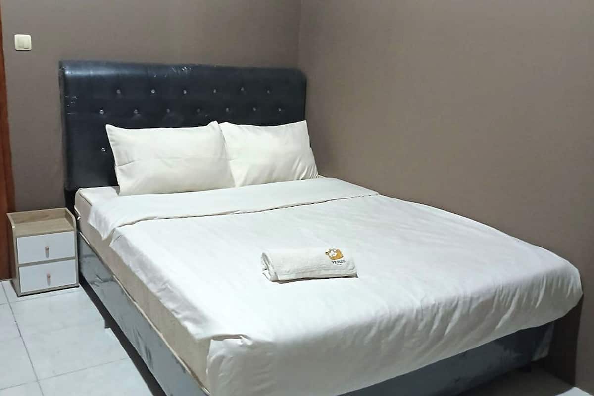 Una cama bien hecha con ropa blanca y una toalla doblada sobre ella.