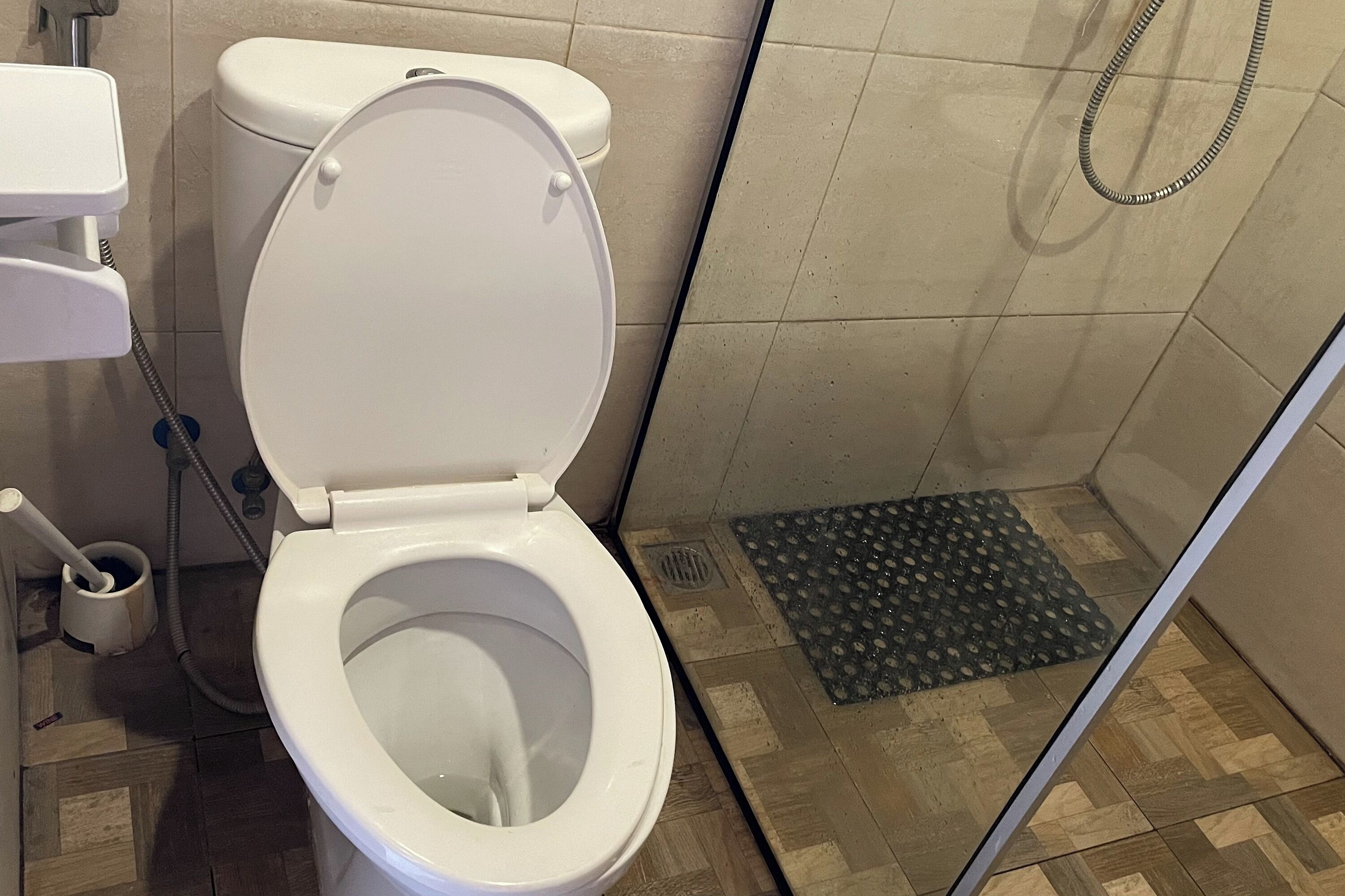 A bathroom with a white toilet, a shower area, and a tiled floor.