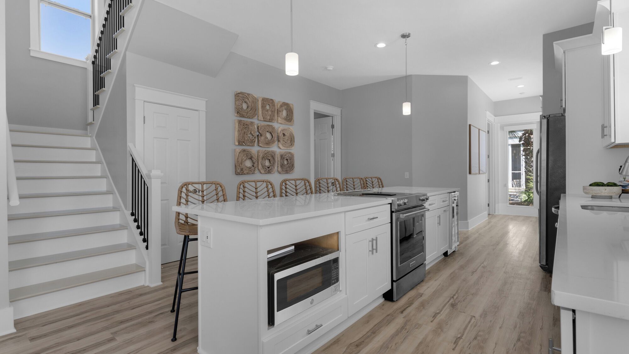 A modern kitchen with a central island, white cabinetry, and a wooden staircase.