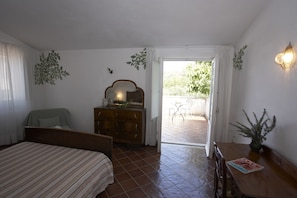 A bedroom with a bed, dresser, and a small table with a magazine. There is a door leading to a balcony with a chair and table outside. - Azienda Agricola Le tore srl (Massa Lubrense)