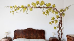 A bedroom with a wooden headboard, a bed with a striped bedspread, two bedside tables with lamps, and a wall-mounted vine decoration. - Azienda Agricola Le tore srl (Massa Lubrense)