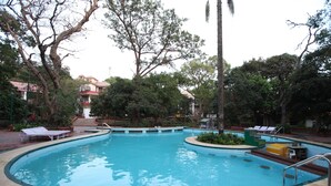 Une piscine à bord incurvé, entourée d’arbres, avec un bâtiment visible au loin.