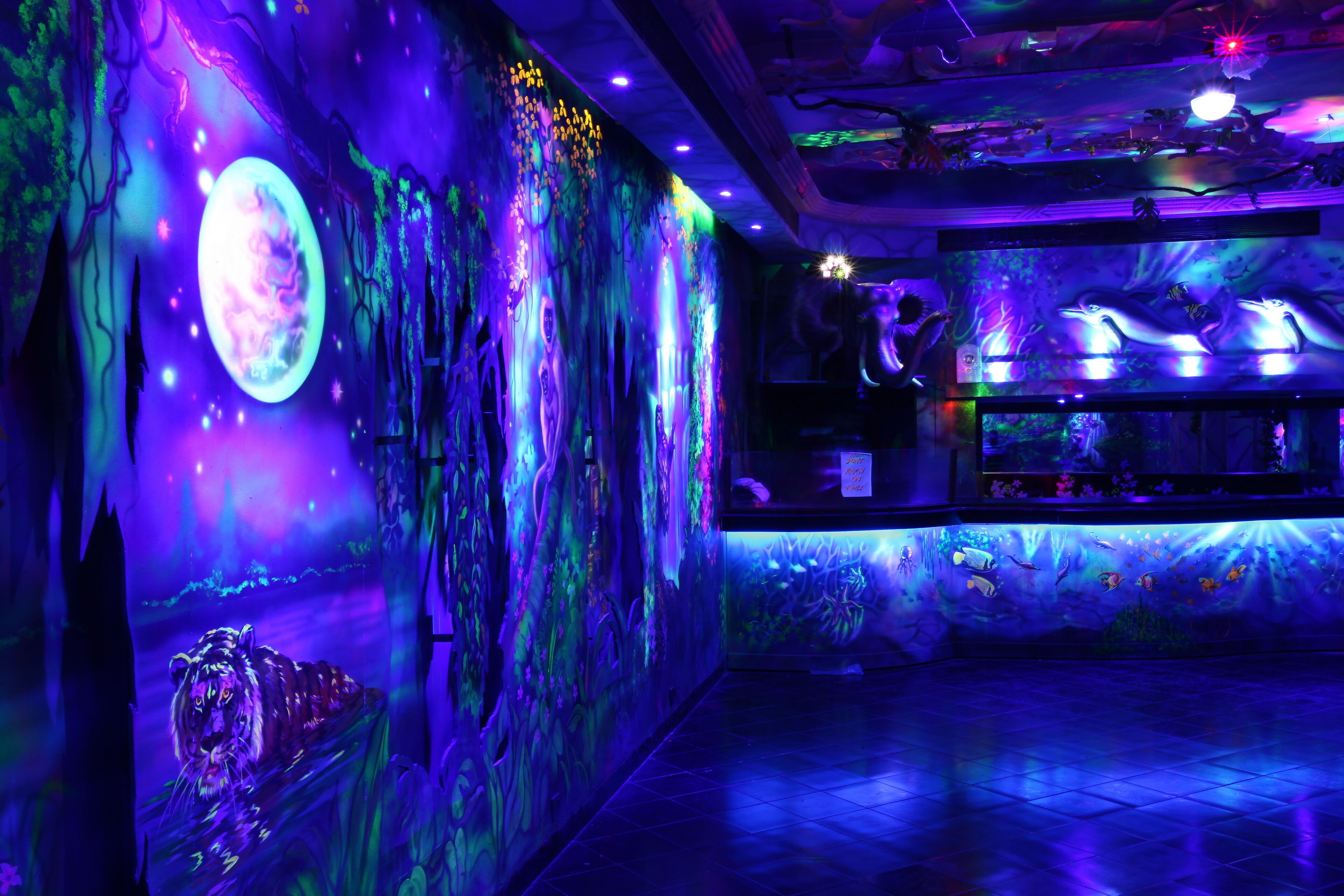 Una habitación con un gran acuario, un mural con una luna brillante y una estatua de tigre.