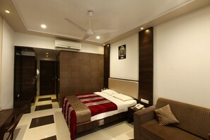 A hotel room with a bed, a sofa, a desk, and a wardrobe. - Usha Ascot (Karjat)