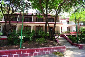 A two-story building with a red and white facade, a central staircase, and surrounding greenery. - Usha Ascot (Karjat)