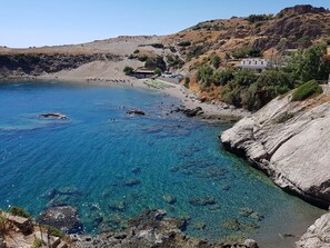 A coastal area with clear blue waters, rocky terrain, and a few buildings.