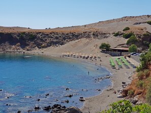 A beach with clear blue water, rocky shore, and a few umbrellas.