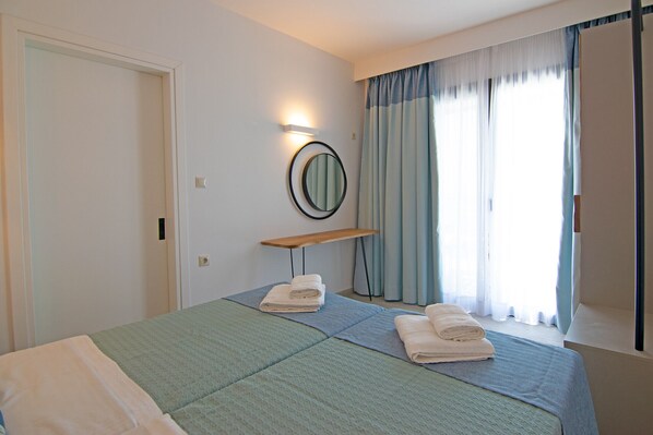 A hotel room with a bed, two towels, a bedside table, a mirror, and a window with curtains.