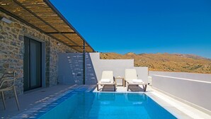 A pool with two lounge chairs, a stone wall, and a view of mountains.