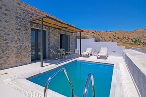 A pool area with a stone wall, a covered seating area, and a view of the hills.
