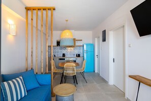 A compact living space with a blue sofa, a dining table with chairs, a kitchen area with a blue refrigerator, and a TV mounted on the wall.