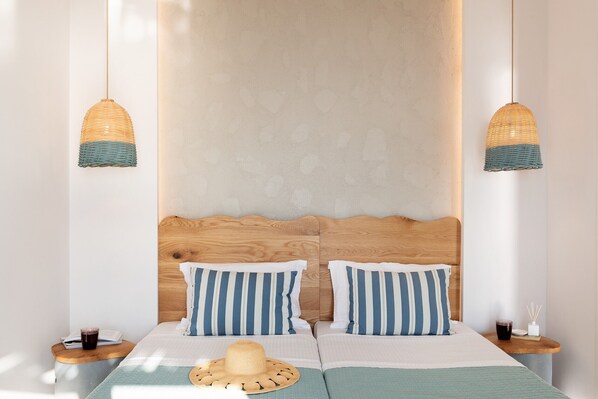 A double bed with striped pillows, a wooden headboard, and two bedside tables with drinks and a hat.