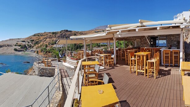A coastal restaurant with outdoor seating overlooking the sea and rocky terrain.