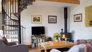 A living room with a fireplace, bookshelves, a TV, and a staircase. - 2 bedroom accommodation in Richards Castle, near Ludlow (Richards Castle, near Ludlow)