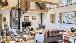 A spacious living area with a wooden staircase, a fireplace, a television, and a dining area with a table set for four. - 2 bedroom accommodation in Richards Castle, near Ludlow (Richards Castle, near Ludlow)