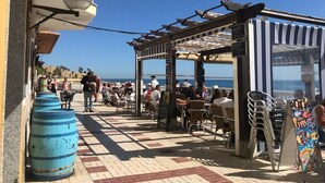 Un espacio al aire libre con mesas y sillas, una pérgola y vista al mar.