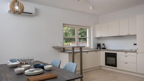 Una cocina moderna con armarios blancos, una mesa de comedor con platos y vasos, y una ventana con vistas a follaje.