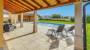 Un patio techado al aire libre con piscina, sillas de descanso y zona de barbacoa.