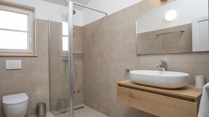Un baño moderno con cabina de ducha de vidrio, un lavabo blanco y un mueble de tocador de madera.