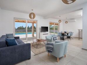 A modern living room with a grey sofa, a light blue armchair, and a dining area with a table and chairs.