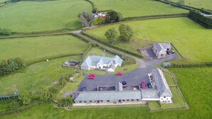 An aerial view of a rural property with a large house, a barn, and several parked cars. - Well Farmhouse - UK11880 (Holsworthy, near Launceston)