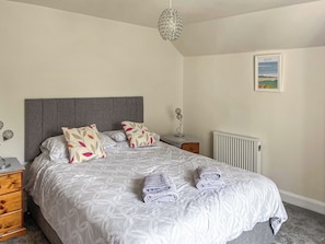 Une chambre à coucher avec un lit, des oreillers, une table de chevet, une lampe, un radiateur et un tableau encadré au mur.